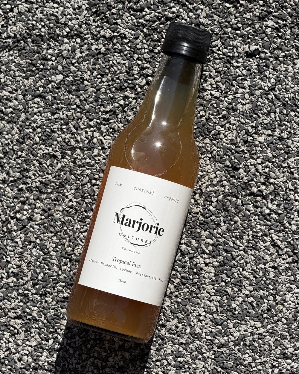 A bottle of Marjorie Cultures Tropical Fizz resting on stone, label facing up.