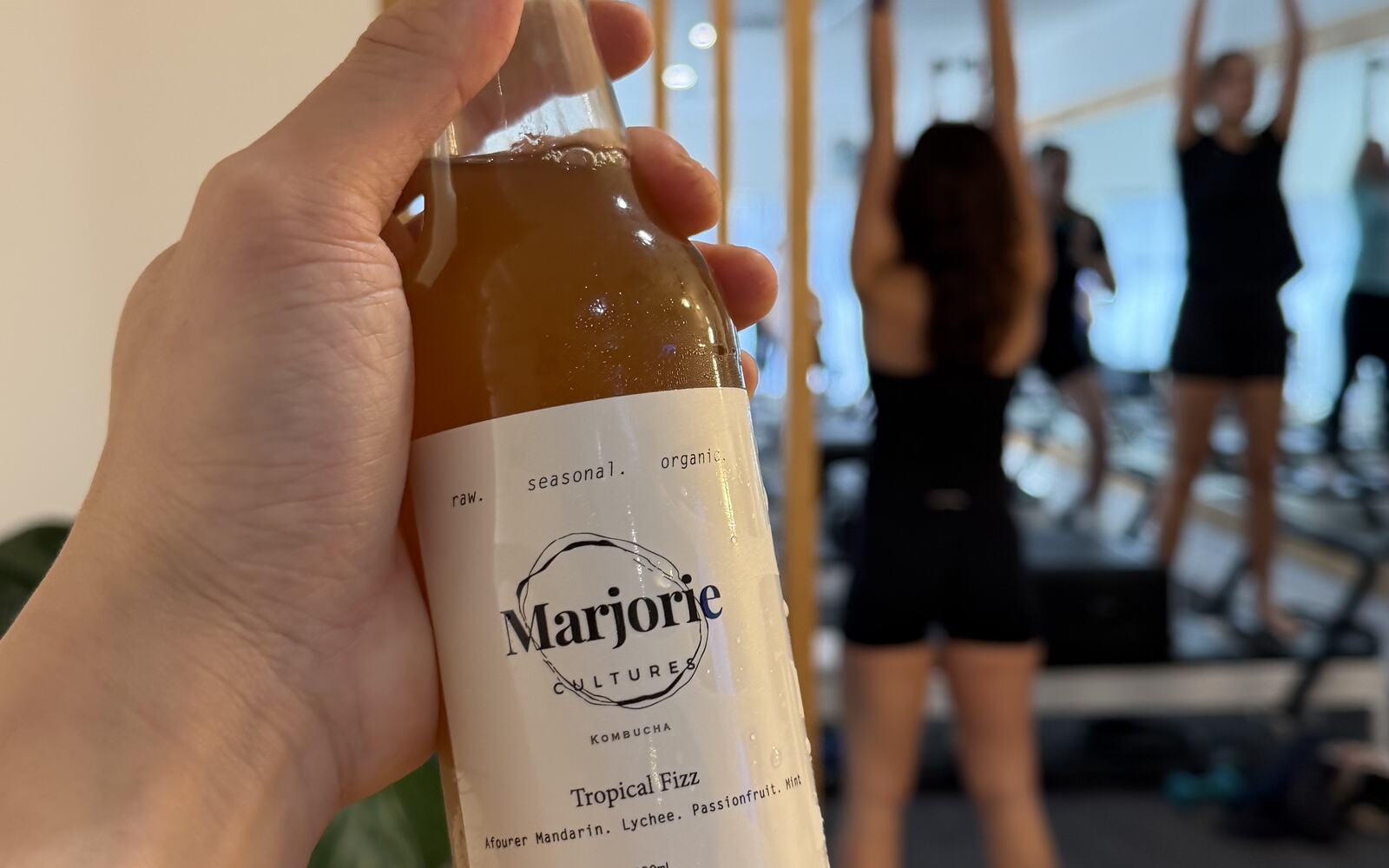 A bottle of Marjorie Cultures held in a pilates studio during a class.